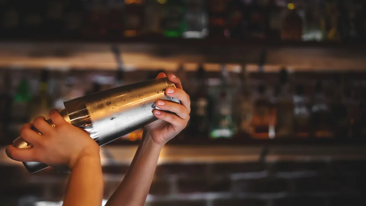 Woman at bar holds steel shaker in her hands, shakes it to make cocktail