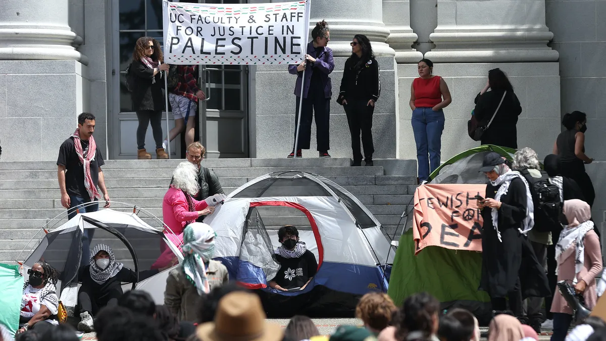 Two protesters hold a sign reading “UC Faculty & Staff for Justice in Palestine” on the steps of a campus building.