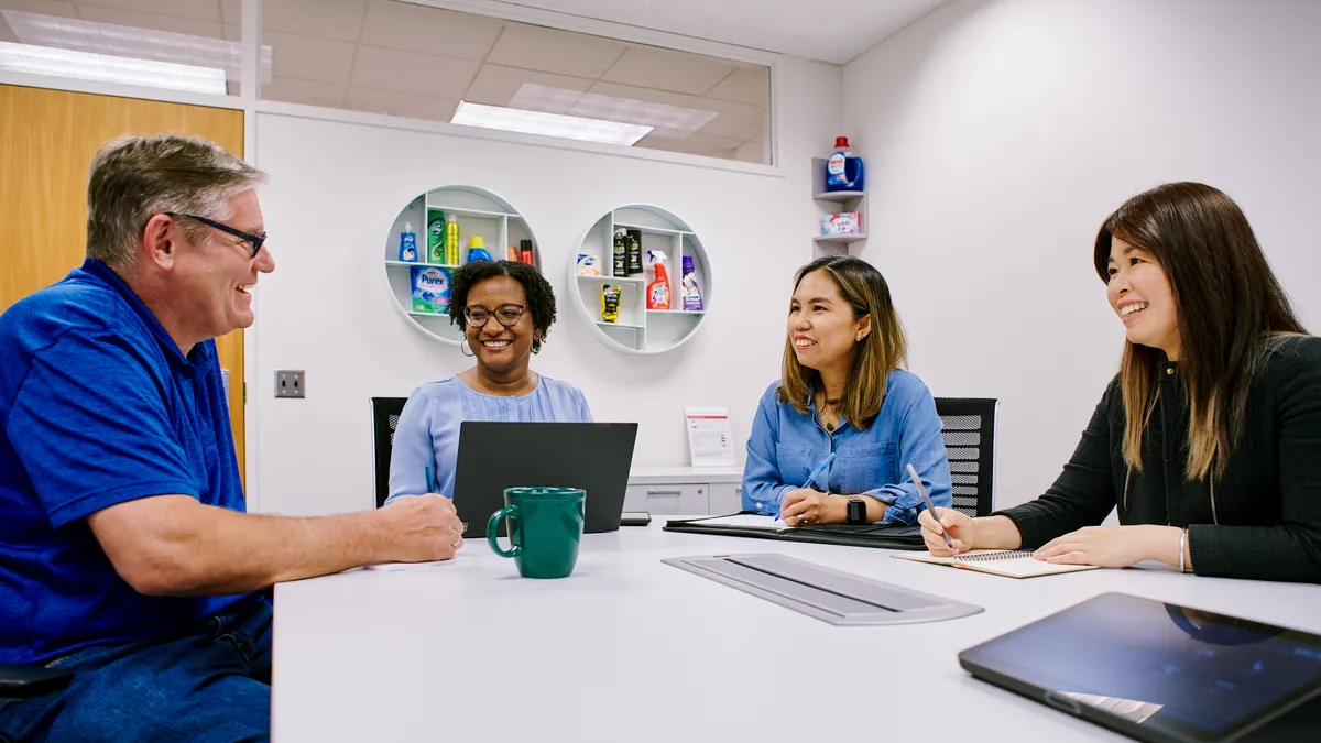 4 workers sitting around an office table smiling.