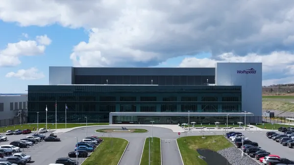 A large building with glass windows facing a parking lot under a sunny sky.
