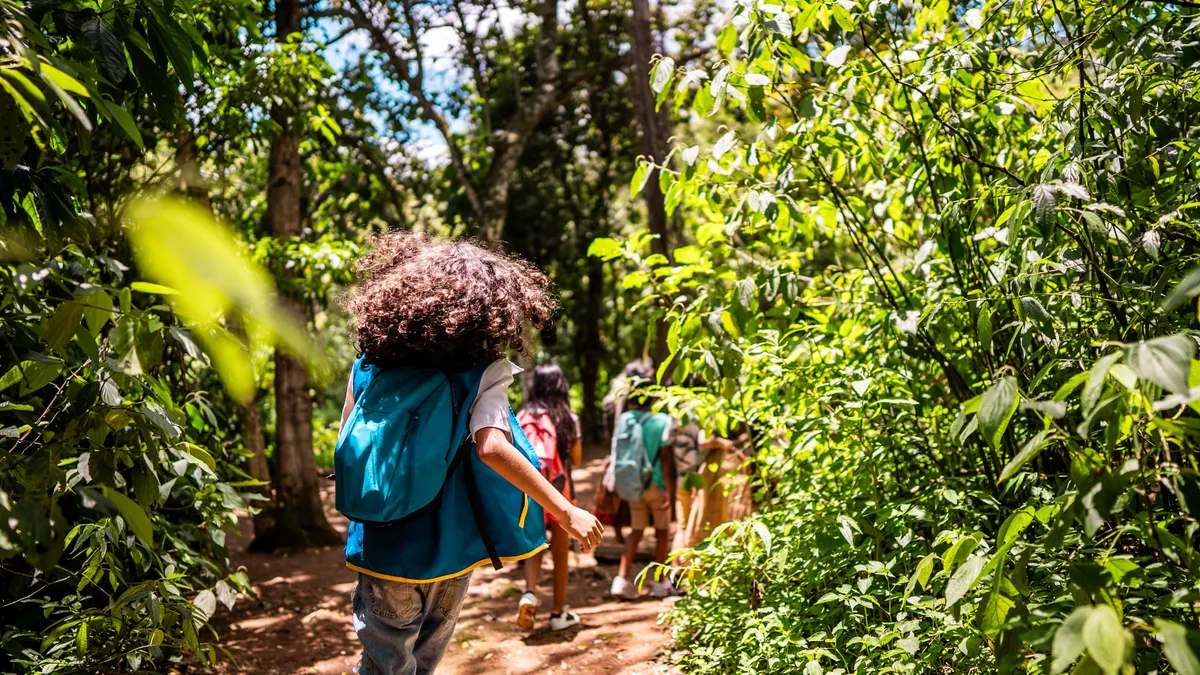 A group of adolescents is pictured hiking a trail through a forest.