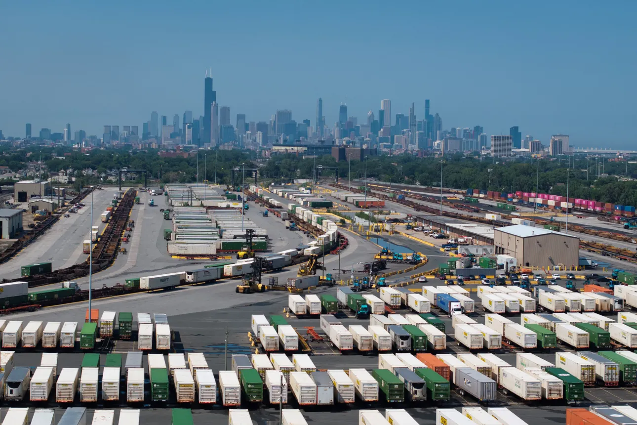 Containers sit near a railroad interchange with te Chicago skyline in the background.