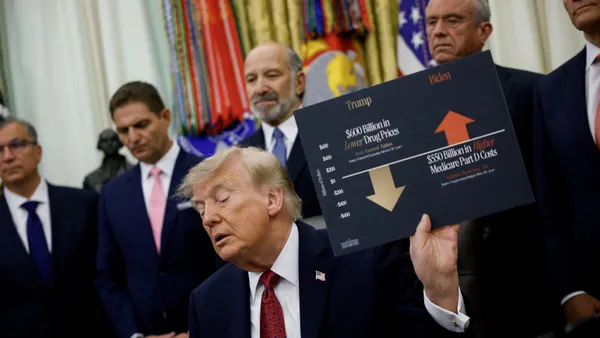 President Donald Trump holds up a chart comparing drug prices and Medicare Part D costs during a healthcare affordability event in the Oval Office.