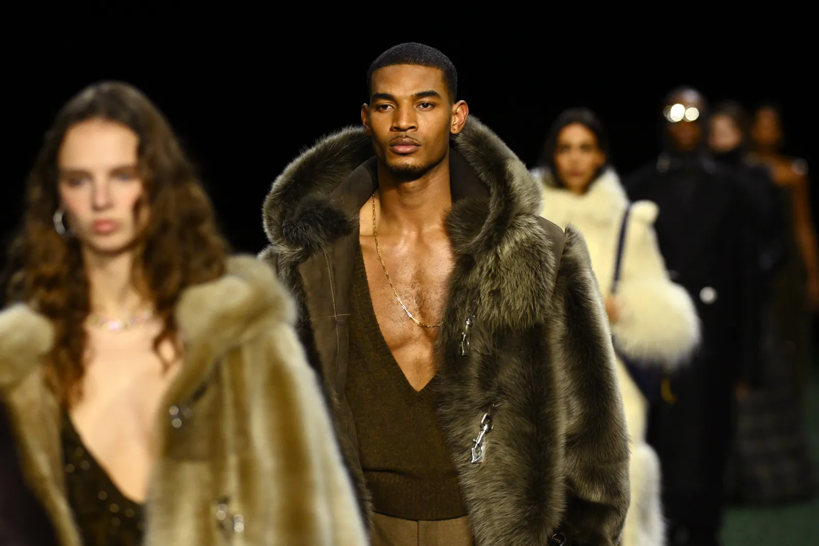 A shirtless model in a fur coat walks down the runway.