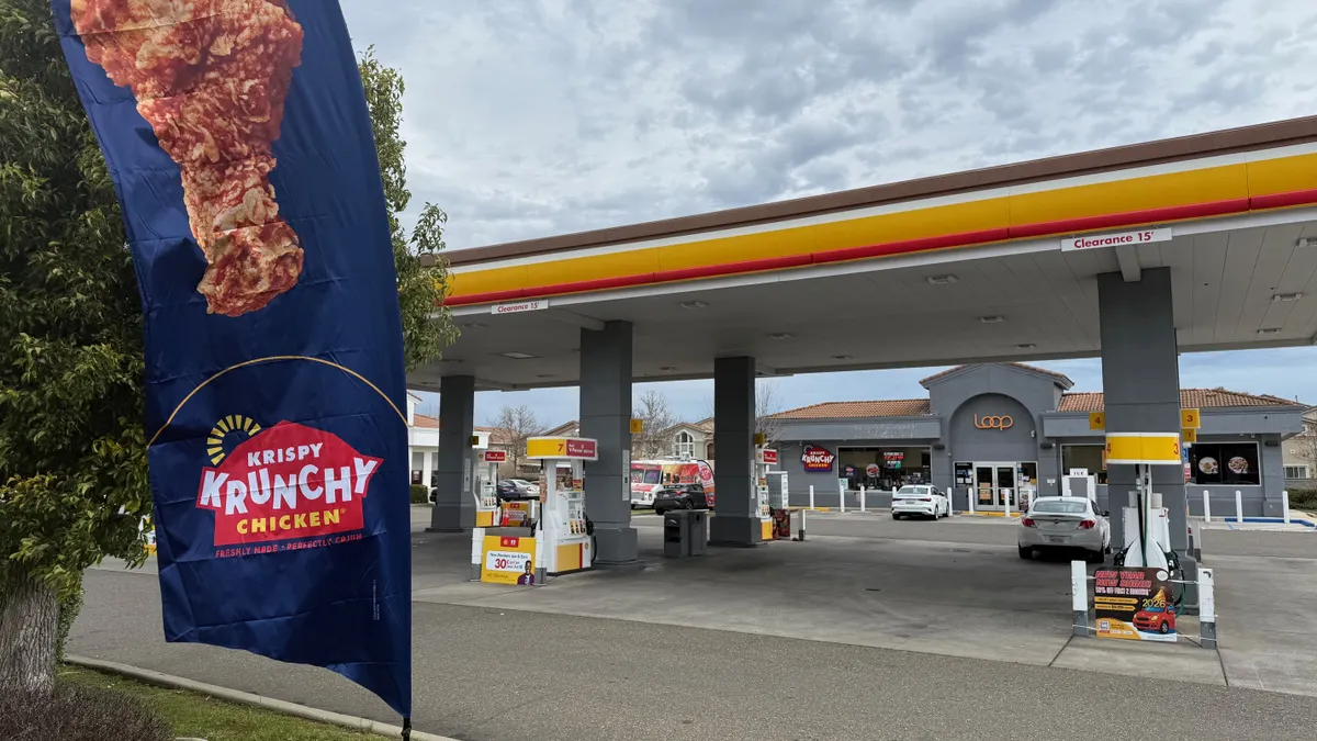 A photo of a flag out in front of a convenience store. The flag says "Krispy Krunchy chicken." A sign over the door of the convenience store says Loop.