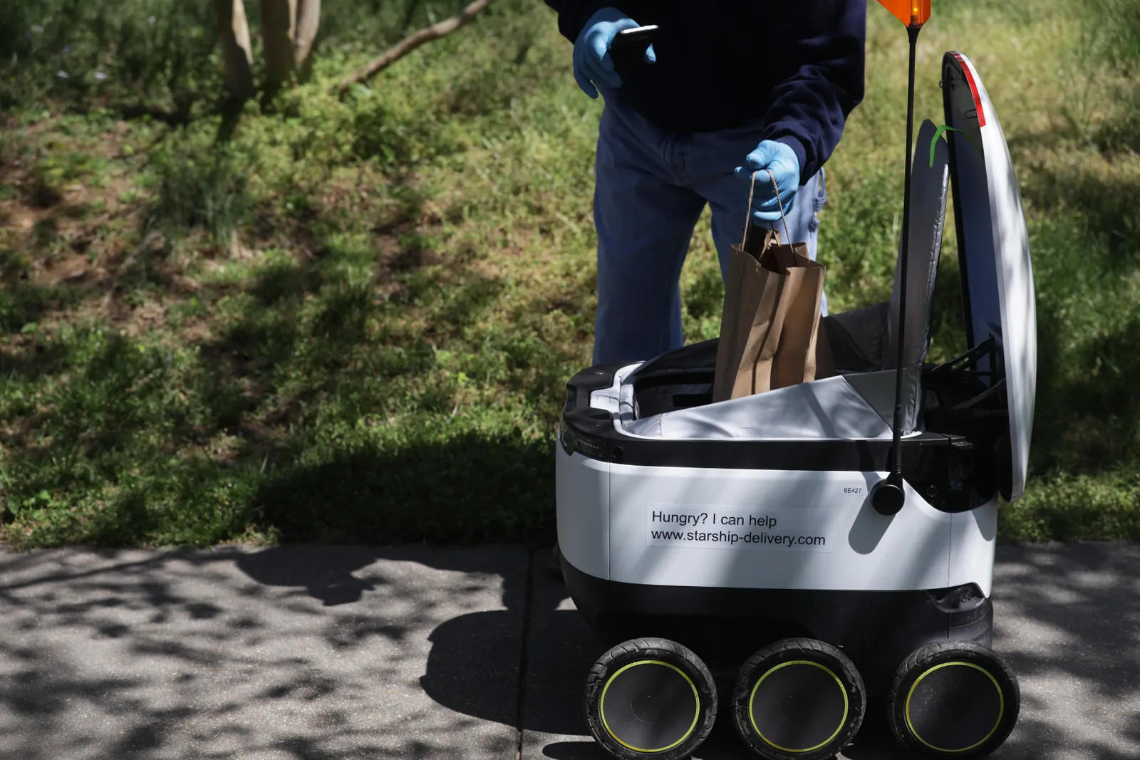 A resident takes out his order from a Starship Technologies delivery robot April 8, 2020 in the Chevy Chase neighborhood of Washington, DC.