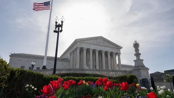 The Supreme Court building is seen from the outside with flowers and a U.S. flag in the forefront