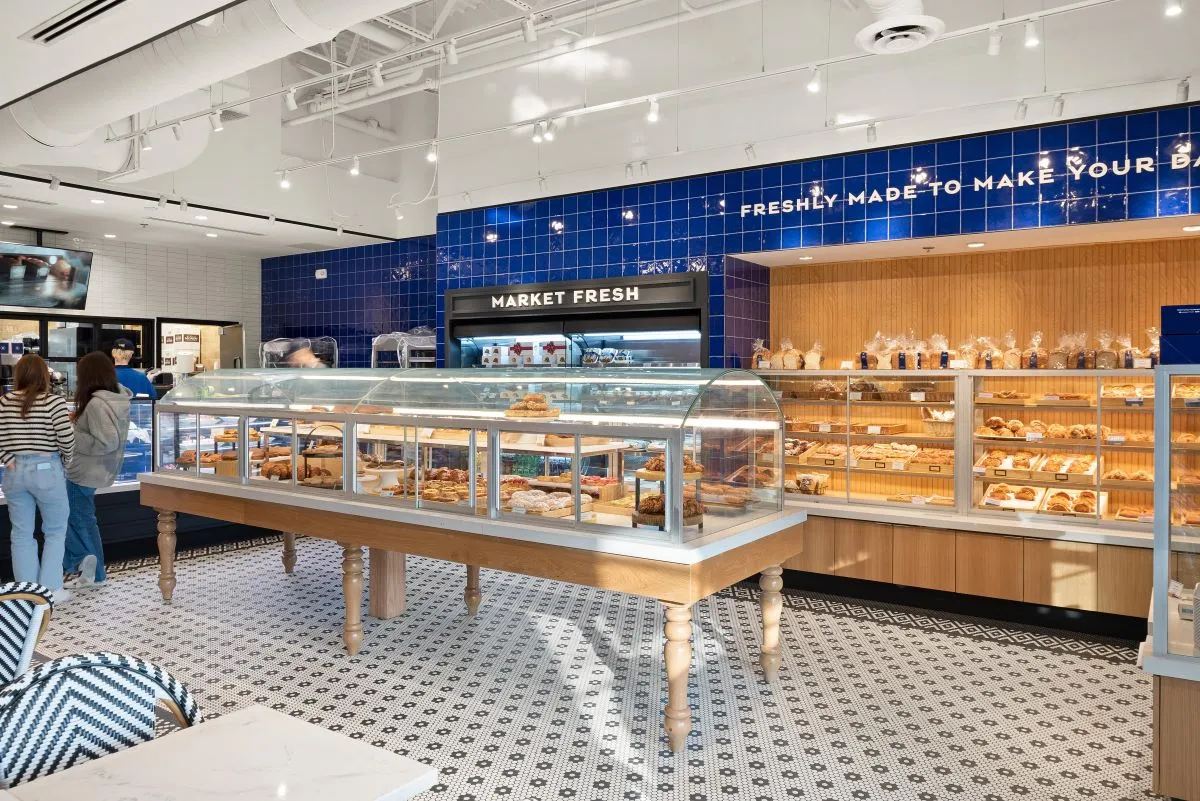 An image of inside a Paris Baguette with a display case in the foreground and breads and a refrigerated case in the background.