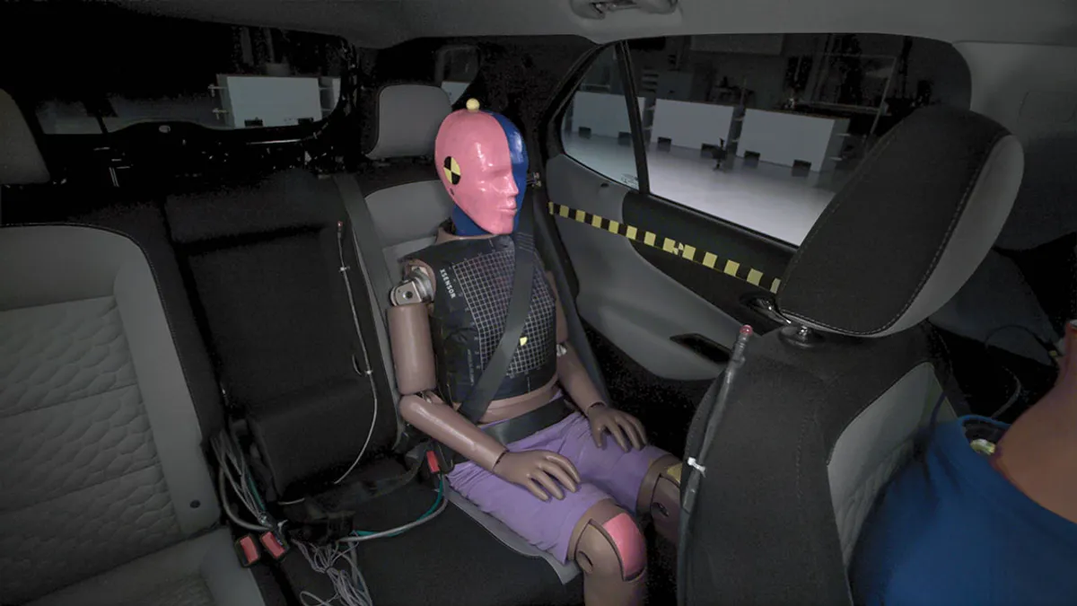 A test dummy placed in the left rear passenger seat of a vehicle for crash testing.