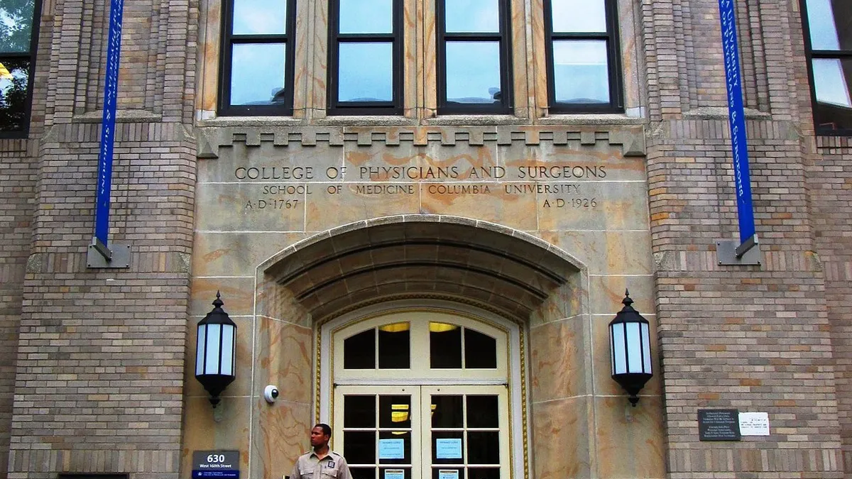 Brown brick front of a building lined with blue streamers. A guard stands in front.