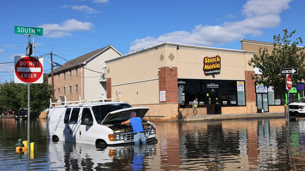 A person attempting to fix a van in a flooded street.