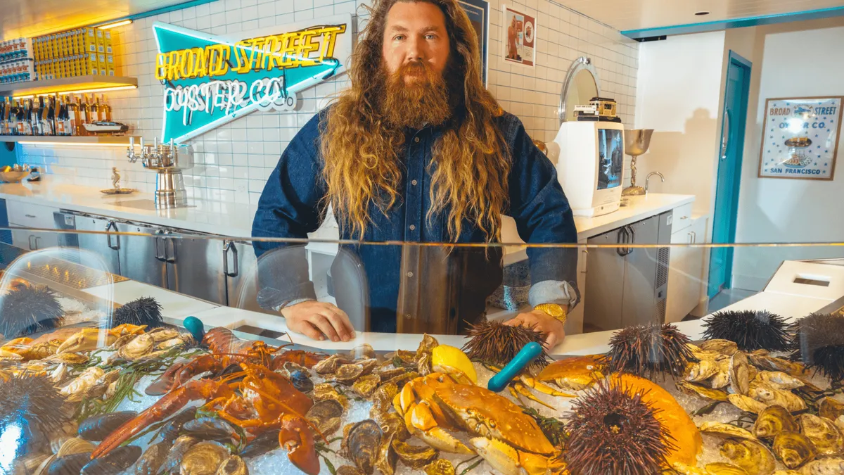 A seafood restaurant owner posing in front of a counter filled with various seafood items.