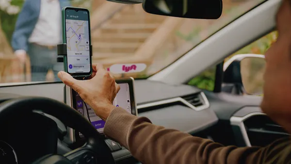 A driver adjusts a smartphone in a holder that shows the Lyft app on the screen.