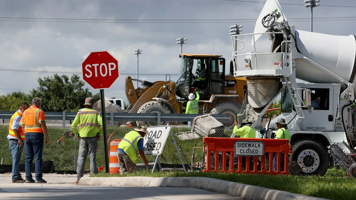 People with heavy machinery wearing safety vests at a road construction site.