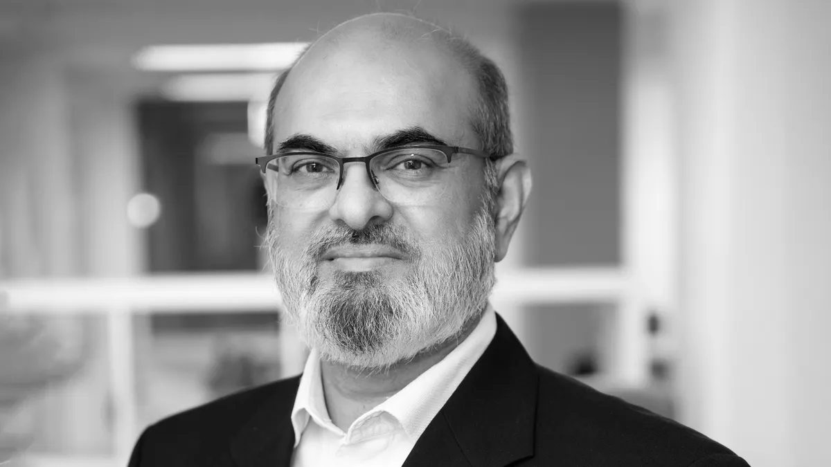 Headshot in black and white of Shahzad Akhtar, a man in a suit with glasses and a beard