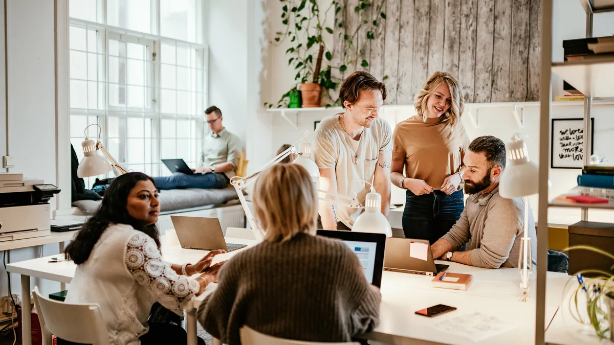 A group of employees work in an office, while another sits on his laptop in the back.