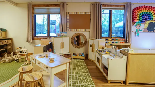 A view into a day care room with wooden kitchen sets, blocks, dolls, and other toys available for play.
