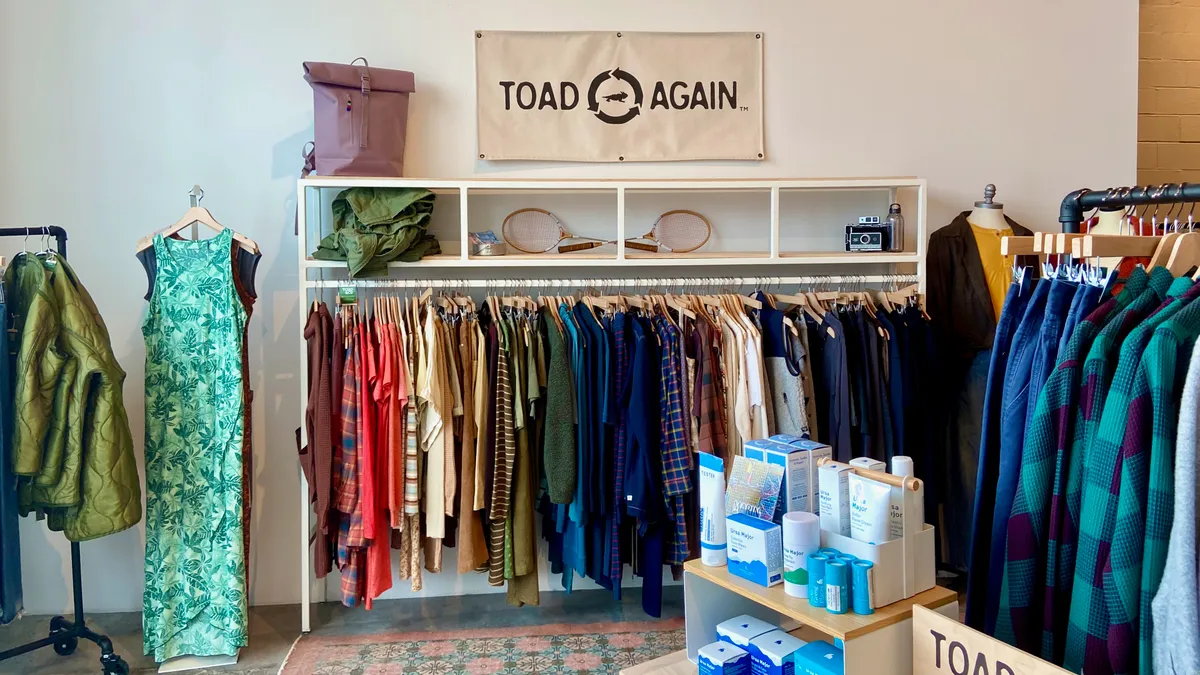 The inside of an apparel store, with clothes hanging on a rack underneath a sign that reads "Toad Again."