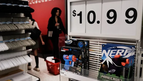 People shop in a store. A large price sign hangs above Nerf guns.