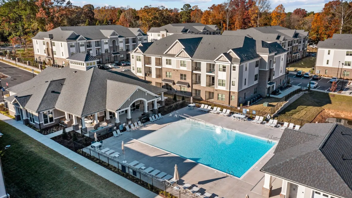 Picture of three-story, brown and white apartments with a pool in the foreground.