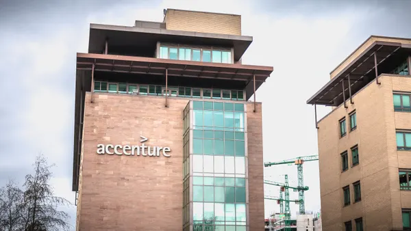 A large building with the Accenture logo is seen in front of trees and construction cranes