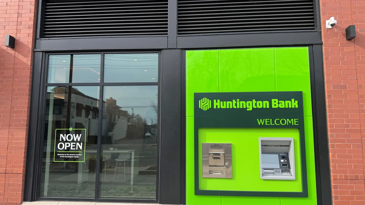 A Huntington Bank ATM sits within a brick and metal building, and a window shows the interior of the branch. Signs read "welcome" and "now open."