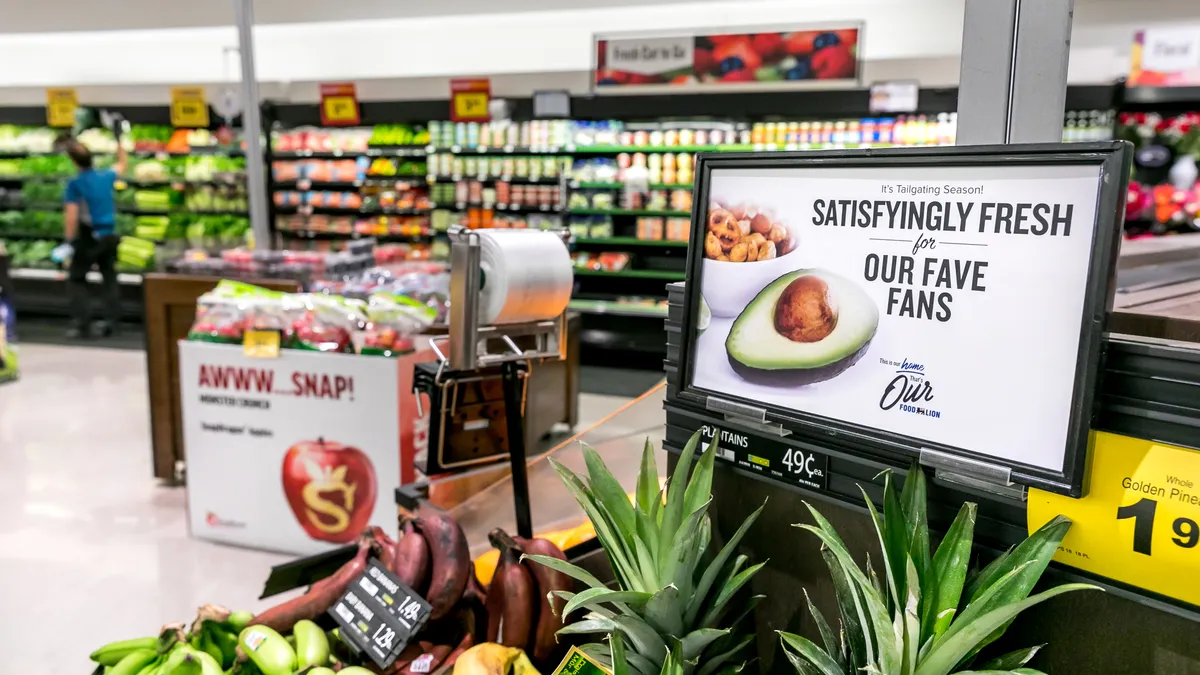 Signs with picture of an avocado says "Satisfyingly fresh for our fave fans" above pineapples and bananas in the foreground.