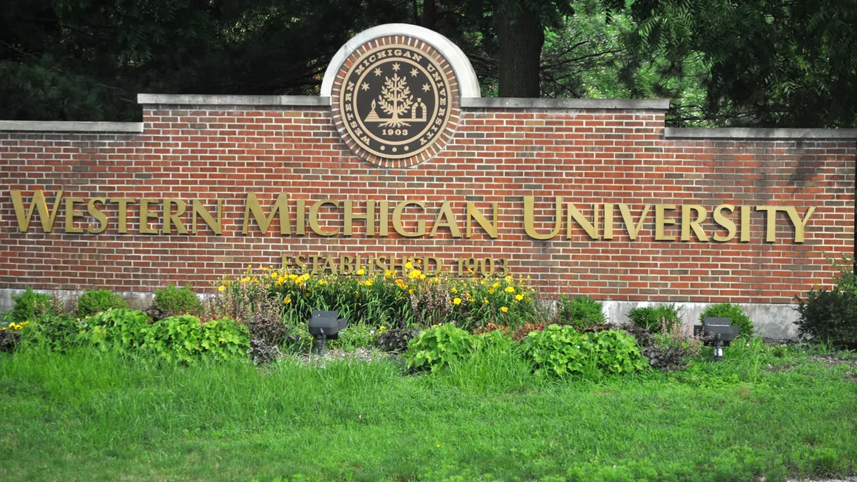 University's welcome sign in gold lettering over brick.