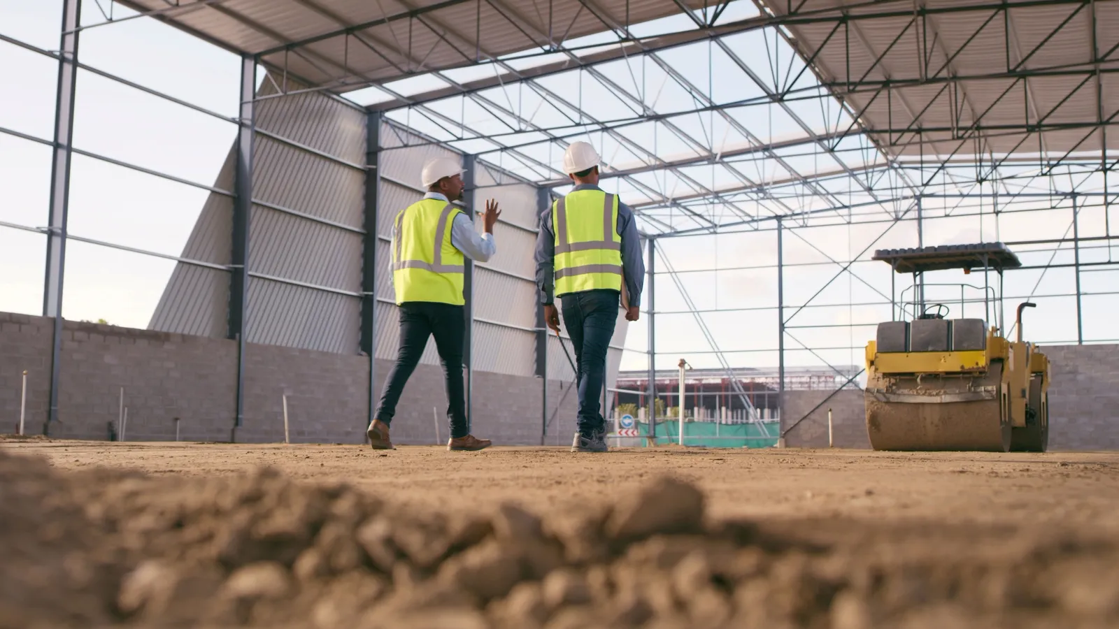 Two people in safety gear walk and talk on a jobsite.