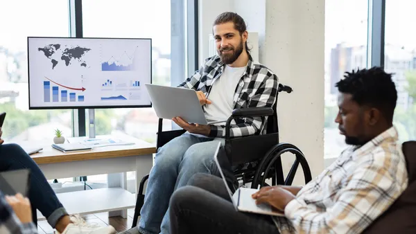 A man in a wheelchair faces a group of people, contributing to the dialogue in a collaborative setting.