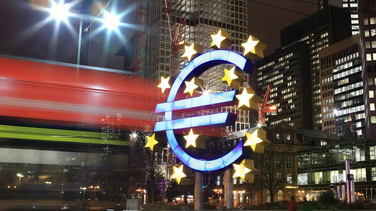 A tram passes the giant Euro symbol with high rise office buildings the city of Frankfurt am, Germany in the background