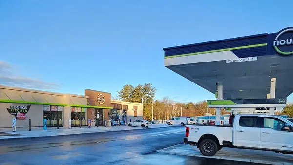 A photo of the exterior of a convenience store, showing the store and fuel canopy. Signs on the canopy and store read "Nouria" while a second sign on the store reads "Nouria's Kitchen/Krispy Krunchy chicken."