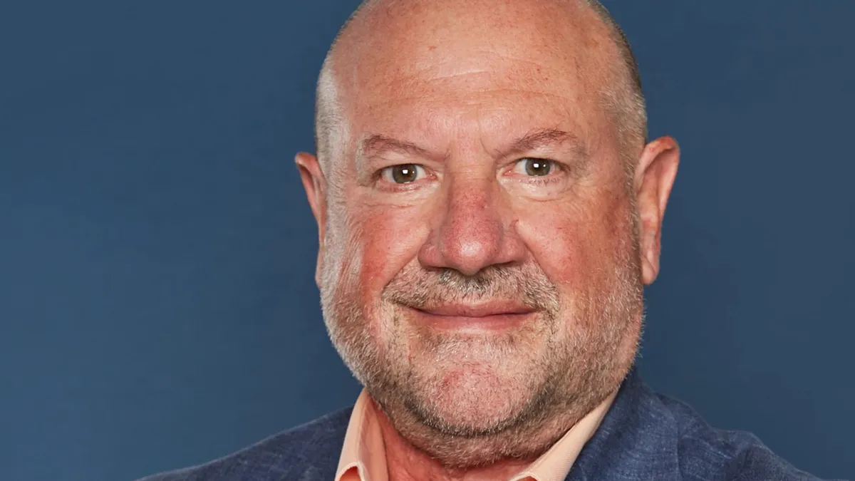 David Persing is wearing a peach-colored button down shirt and blue blazer in a professional photo.