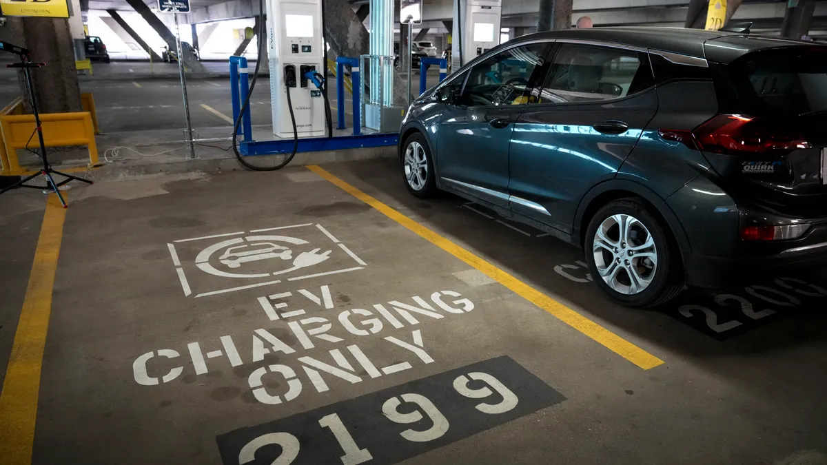 An empty EV charging station space next to a car charging in a parking garage