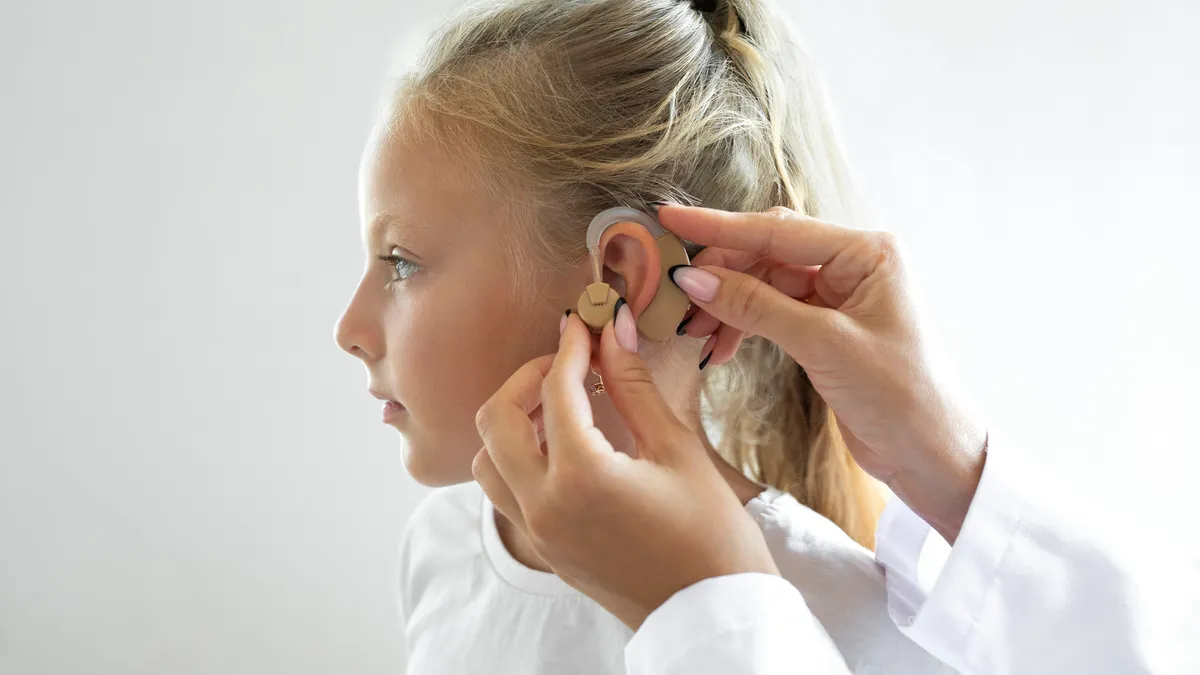 A physician places a hearing aid in a child's ear.