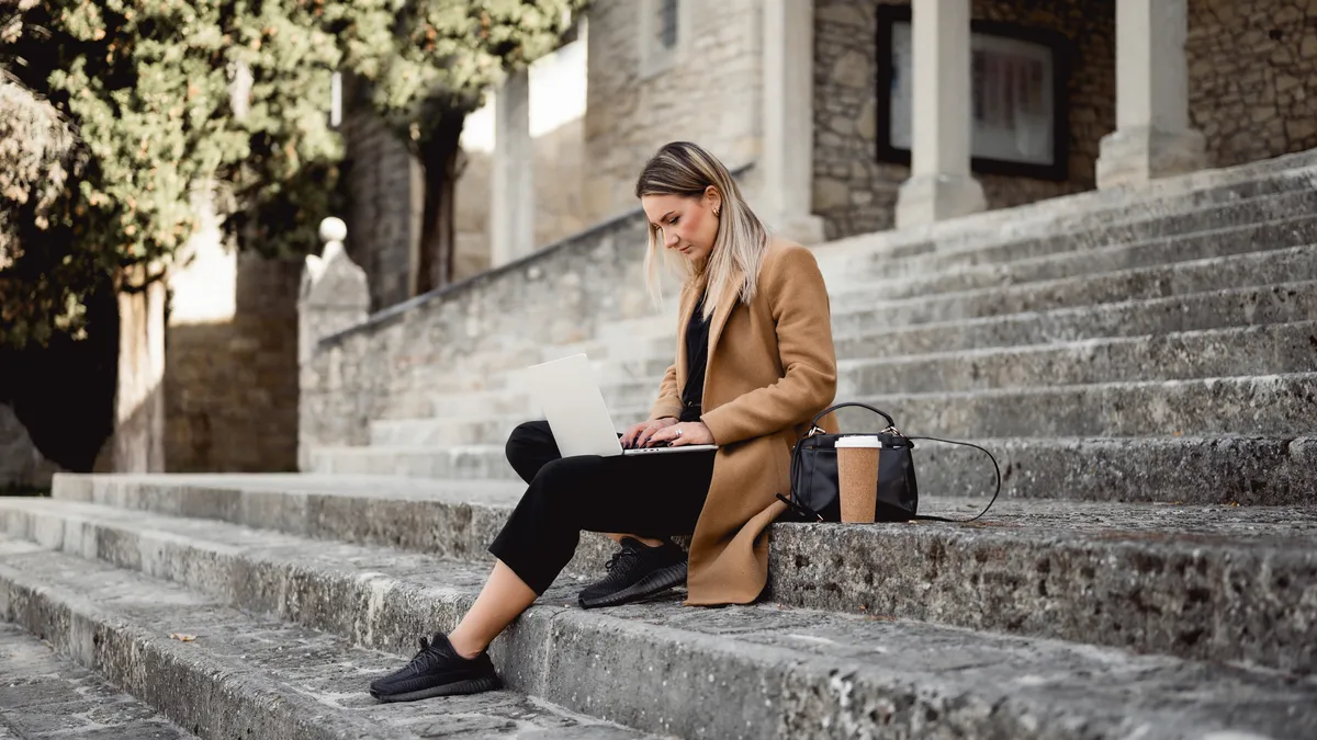 Side view of a young woman studying outdoors on a stairs of a university campus.