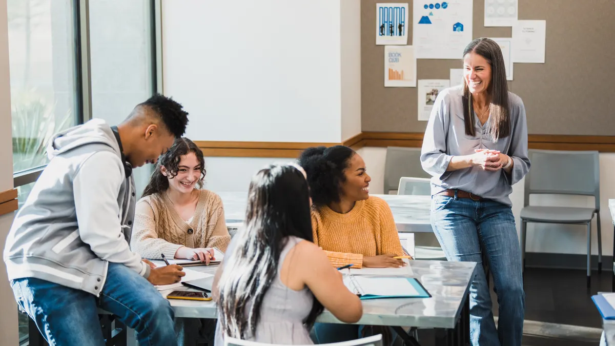 A teacher engages with four teenage students seated at a table in a classroom.