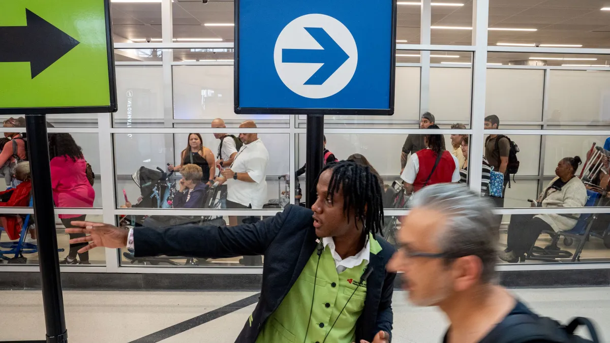 An airport employee directs customers through security screenings.