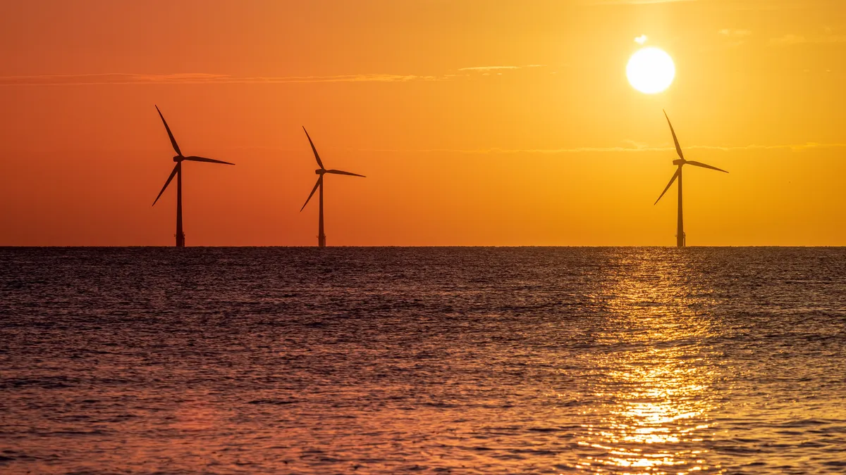 Offshore wind farm turbines silhouetted against an orange sunrise.