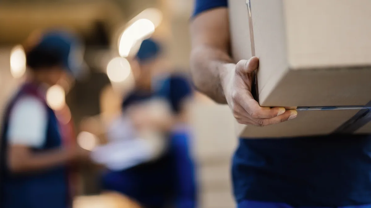 Hands carry a cardboard box with other workers blurred in the background