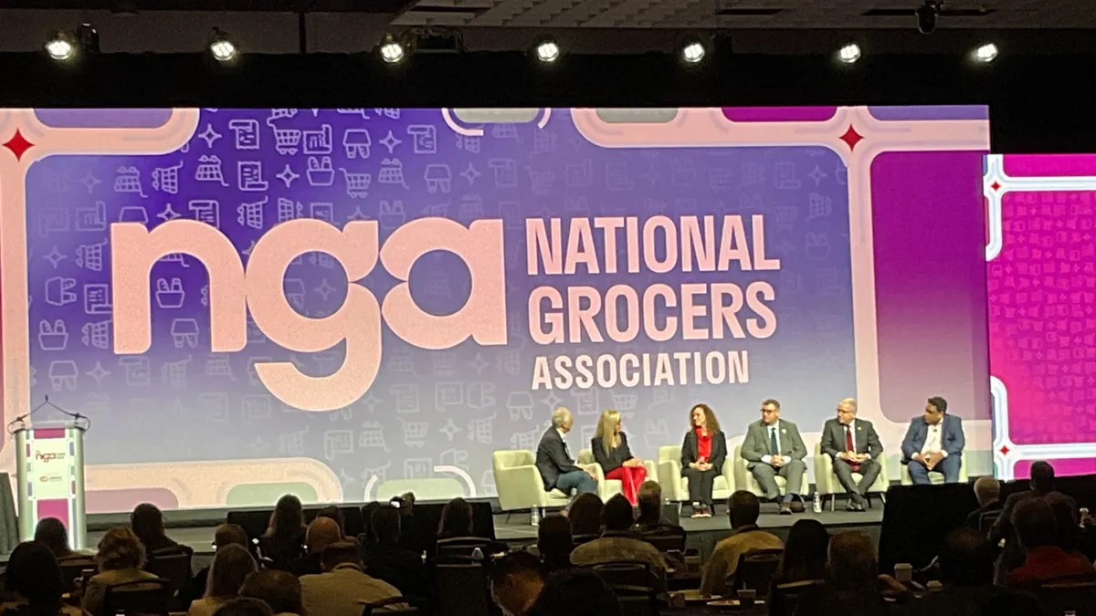 People sitting on a stage in front of a sign that says "National Grocers Association."
