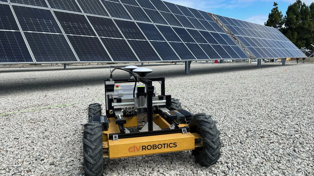 A small yellow robot with wheels, developed by Civ Robotics. It sits in front of solar panels and is positioned on top of stones.