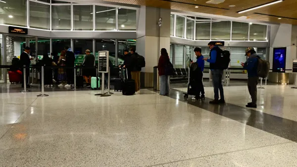 People stand in line to board a green bus seen through a glass partition.