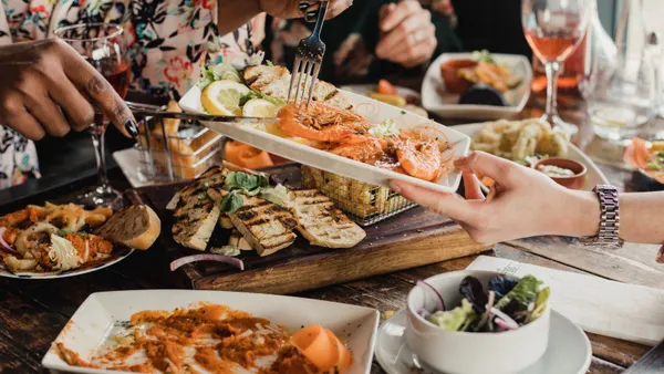 A photograph of two arms holding up a plate of prawns above a wooden table full of food.