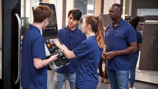Four people in dark purple polo shirts working on a CNC machine.