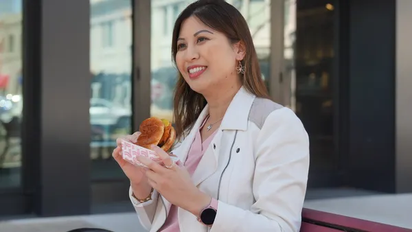 A photo of a person walking in front of a store holding a chicken sandwich.