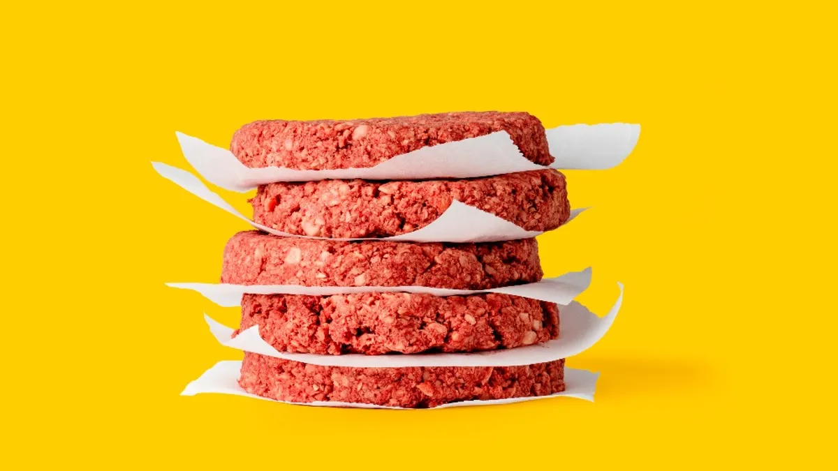 A stack of uncooked Impossible Burger patties separated by wax paper on a yellow background