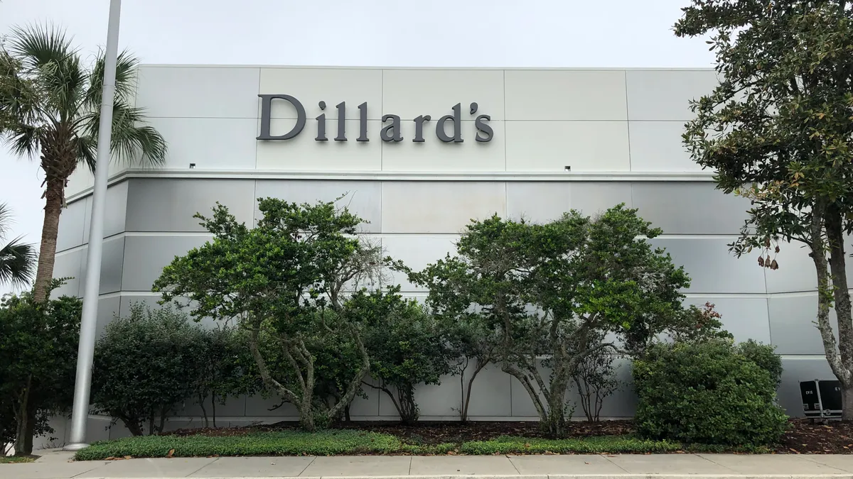 Trees with dark green leaves frame the light-gray stone exterior of a Dillard's department store.