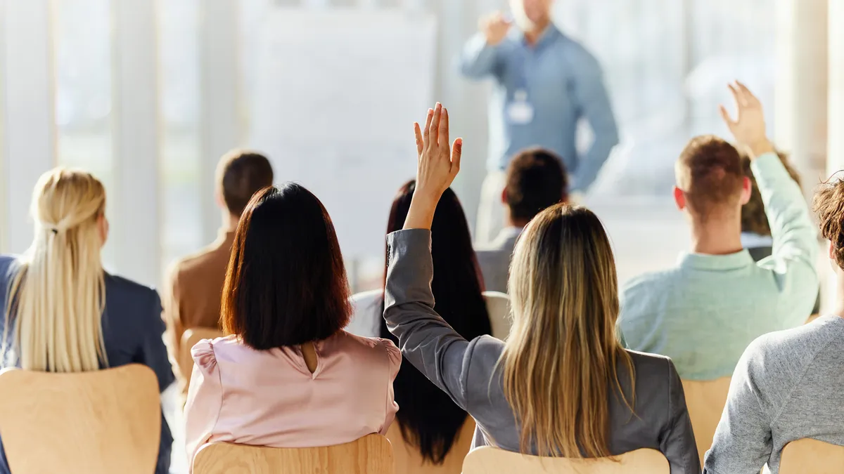 Rear view of a people raising their hand to ask a question at a work event in the board room.