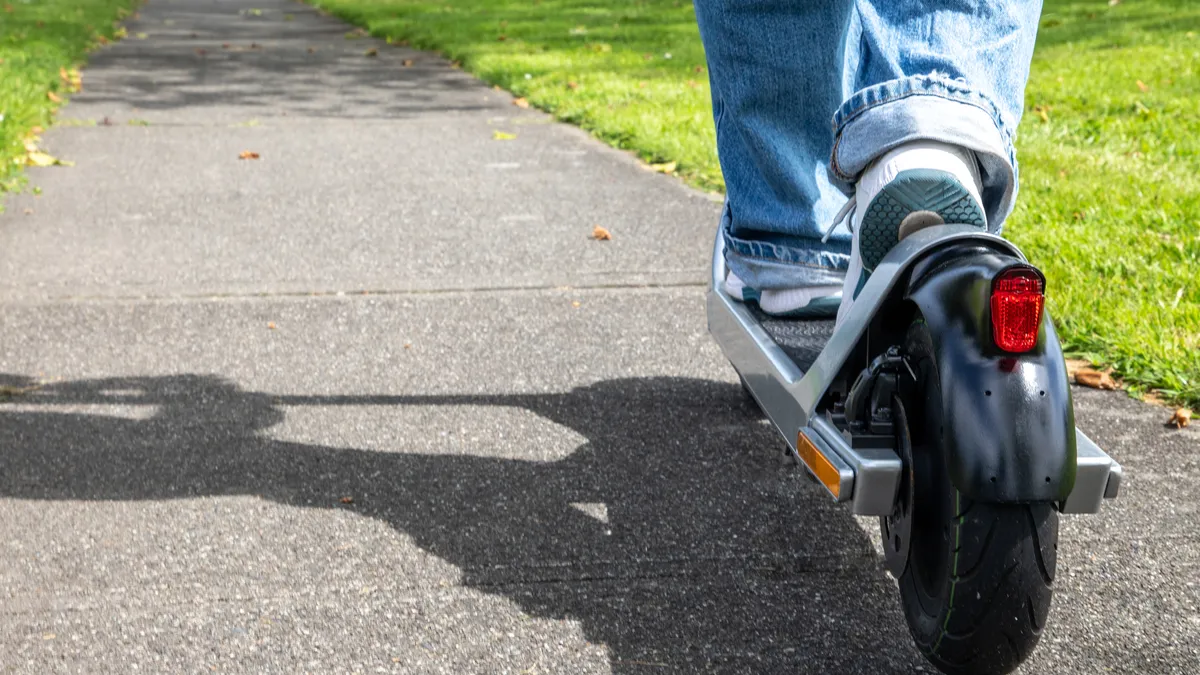 A person rides an electric scooter on a sidewalk.